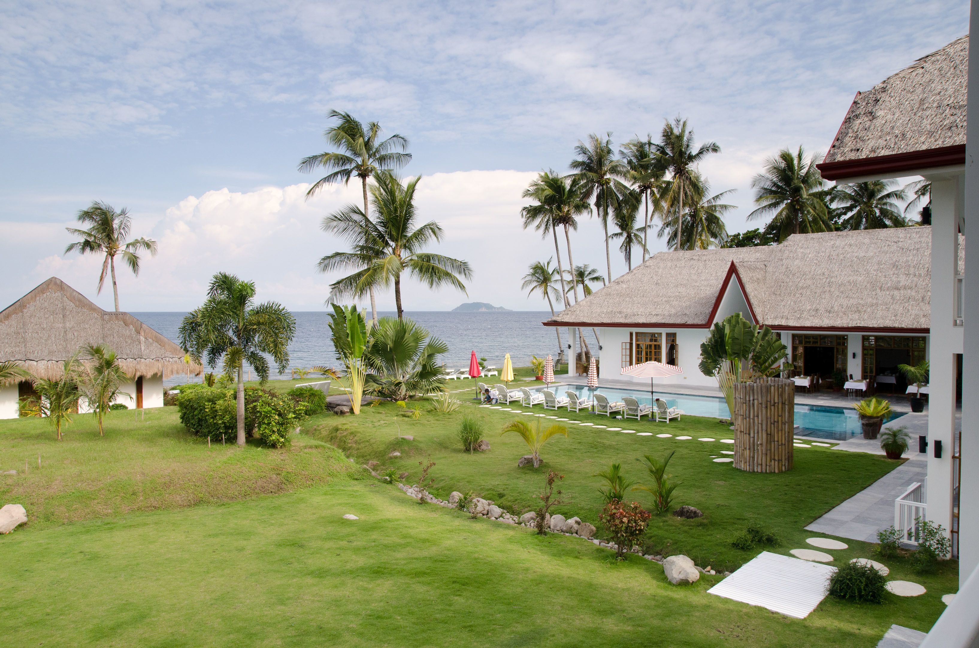 Ein Resort mit Pool, Liegestühlen, Palmen und Blick auf den Ozean.