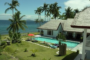 A pool area with lounge chairs and umbrellas, surrounded by palm trees and a view of the ocean. - Sea Dream Resorts (Dauin)