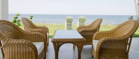 A wicker lounge area with a view of the sea and a palm tree.