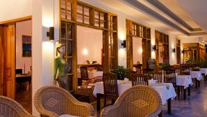 A restaurant with wicker chairs and tables, wooden partitions, and wall-mounted lights.
