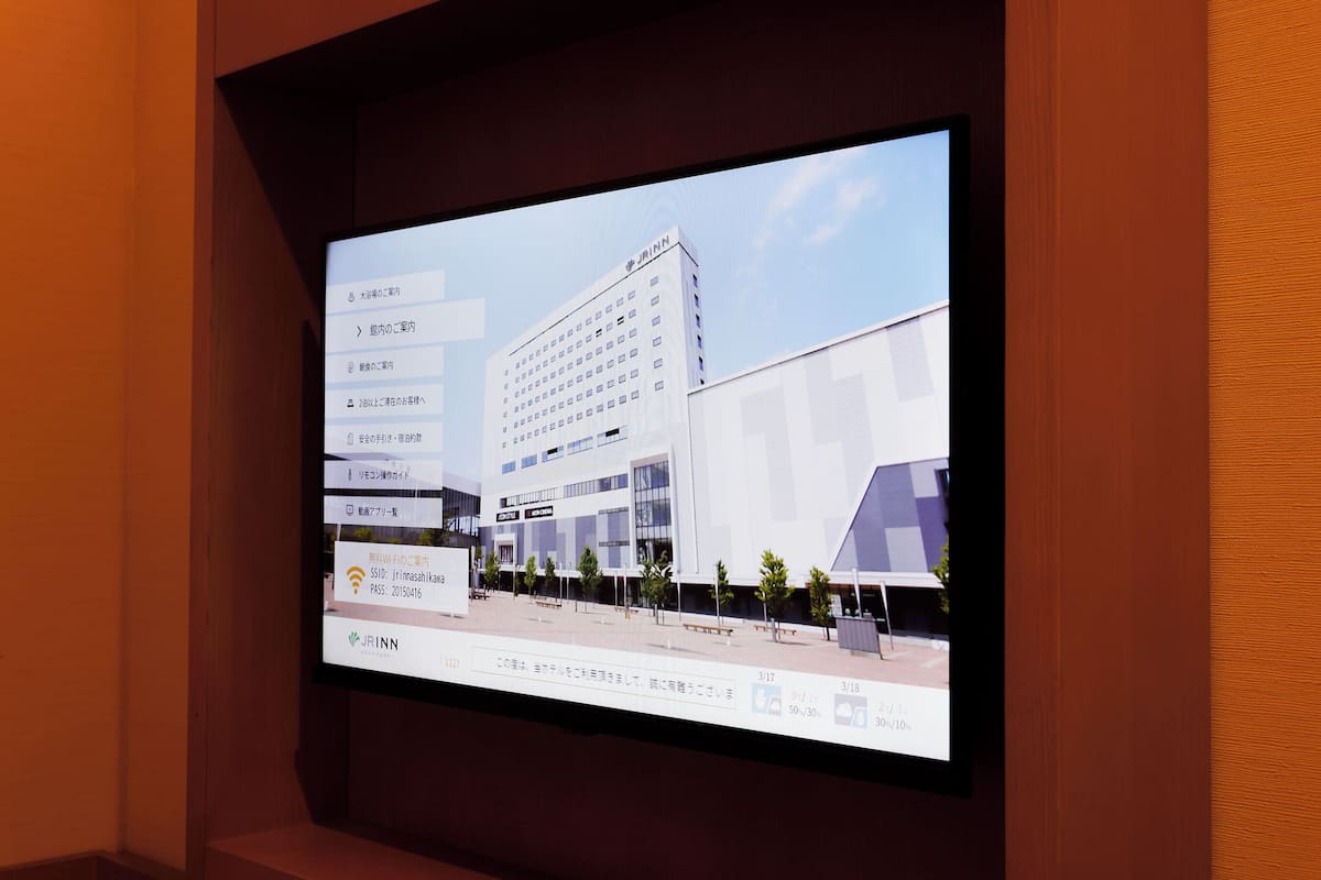 A digital display of a modern building with multiple floors, a flat roof, and a parking area with trees.