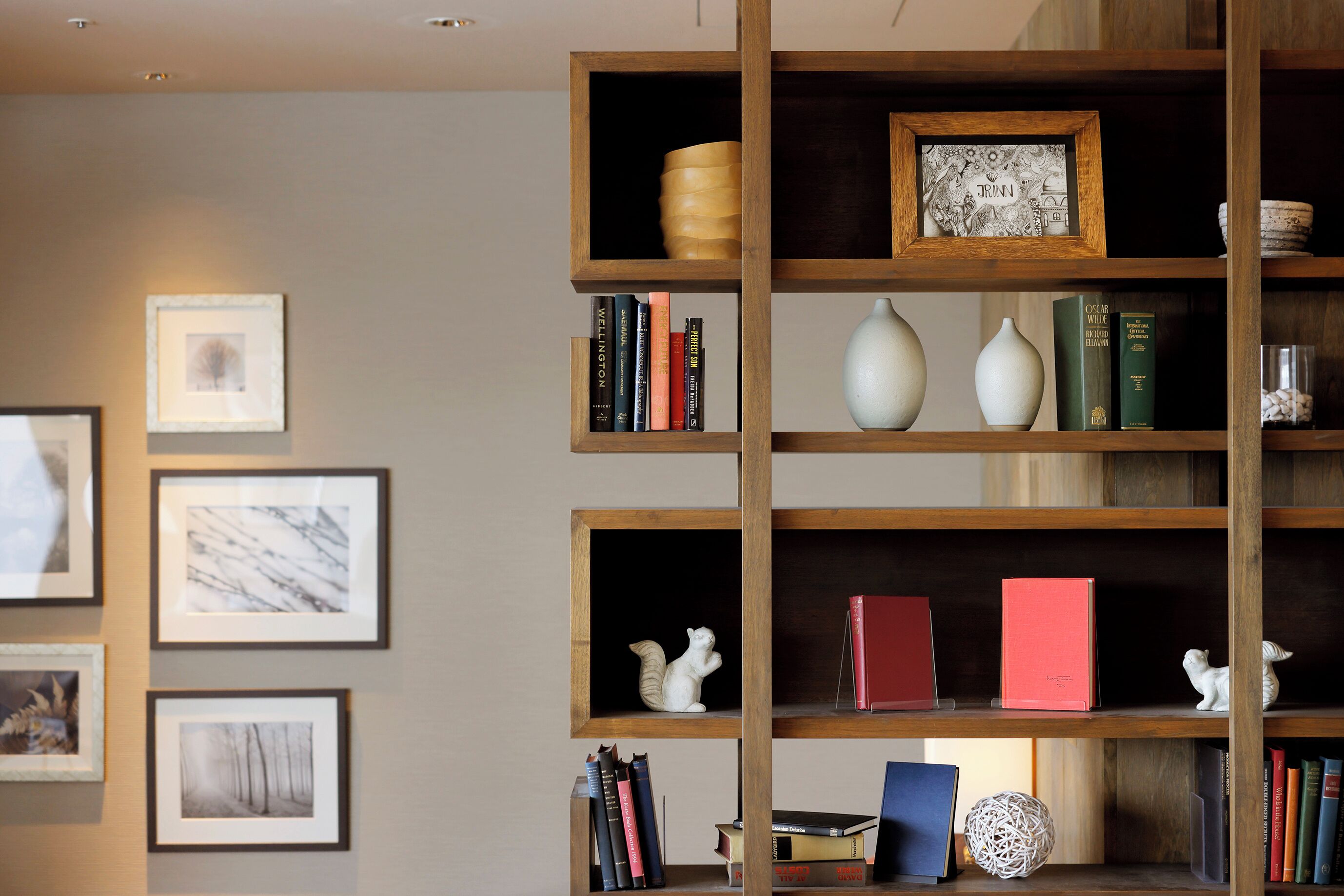 A room with wooden bookshelves containing books, decorative items, and framed pictures.