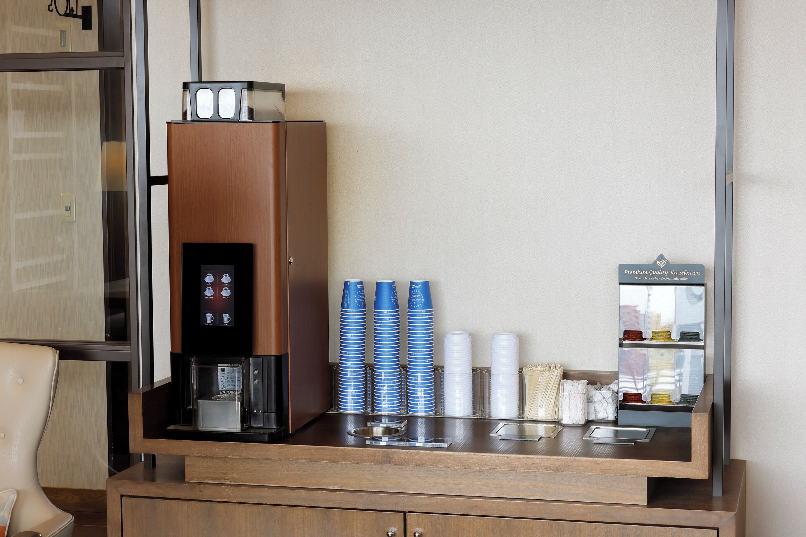 Un espace d’accueil d’hôtel comprenant une machine à café, des piles de tasses et un distributeur de boissons.