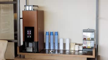 Un espace d’accueil d’hôtel comprenant une machine à café, des piles de tasses et un distributeur de boissons.