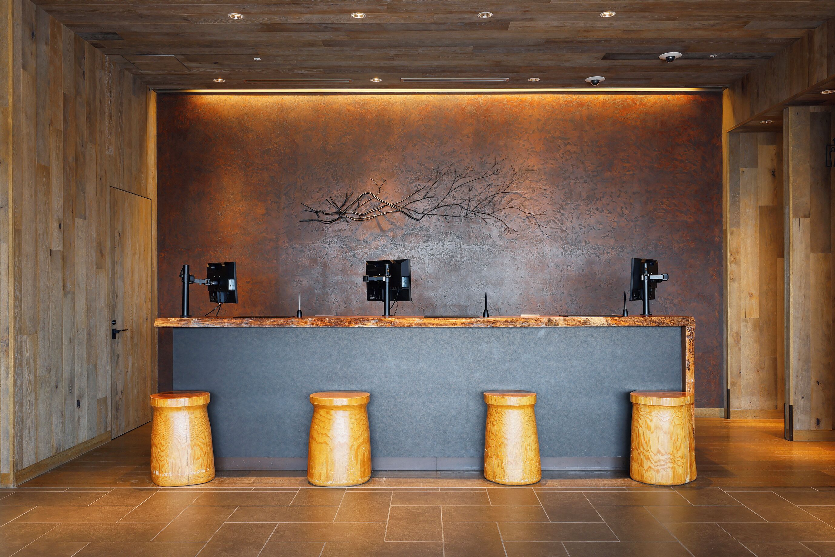 A reception area with a wooden reception desk, two black speakers, and three wooden stools.