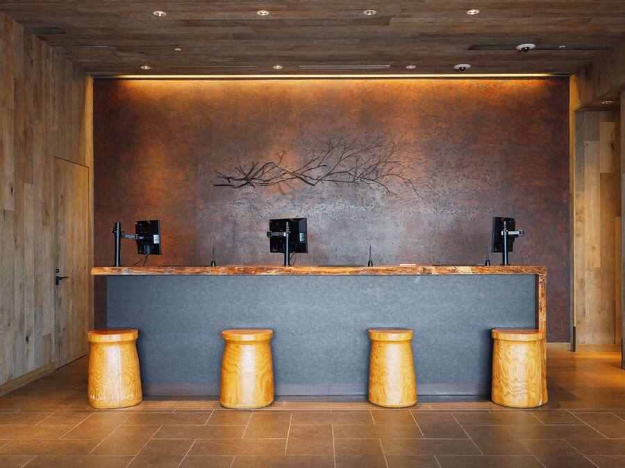 A reception area with a wooden reception desk, two black speakers, and three wooden stools.