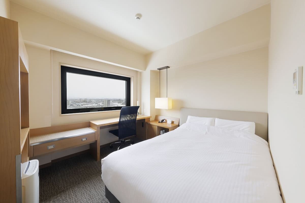 Une chambre d’hôtel équipée d’un lit, d’un bureau, d’une chaise et d’une fenêtre donnant sur la ville.