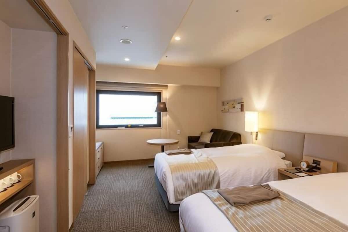 Camera d'albergo con due letti, televisione, scrivania, sedia, un tavolino e una finestra.
