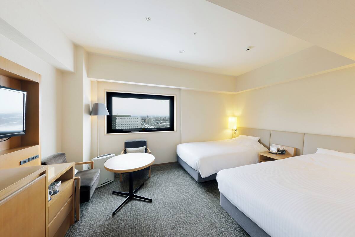 A hotel room with a bed, a desk, a chair, a TV, and a window with a city view.