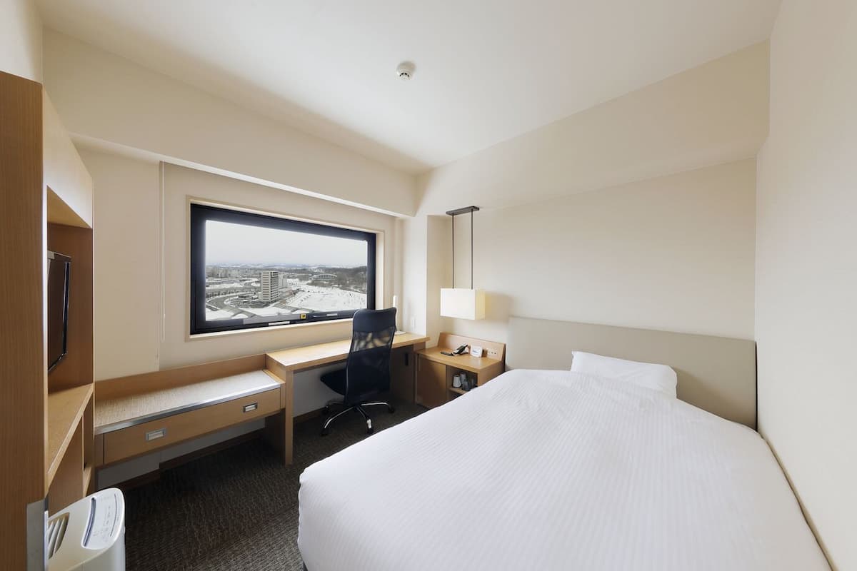 Une chambre d’hôtel équipée d’un lit, d’un bureau, d’une chaise et d’une fenêtre donnant sur la ville.