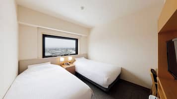 A hotel room with two beds, a window with a city view, a small bedside table with a lamp, and a television on the right.