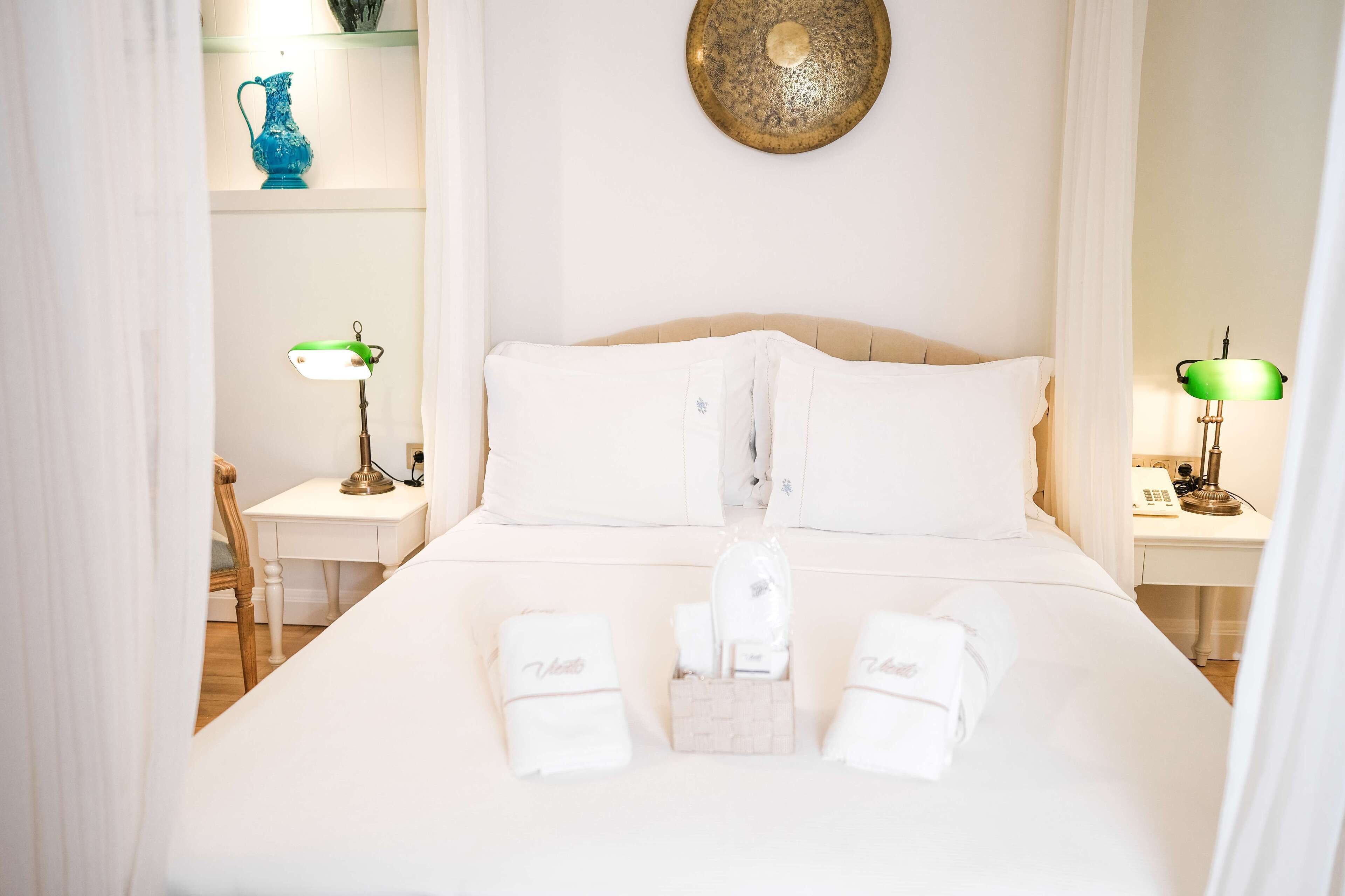 Una cama bien tendida con ropa de cama blanca, una mesita de noche con lámpara y un plato decorativo en la pared.