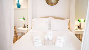 Una cama bien tendida con ropa de cama blanca, una mesita de noche con lámpara y un plato decorativo en la pared.