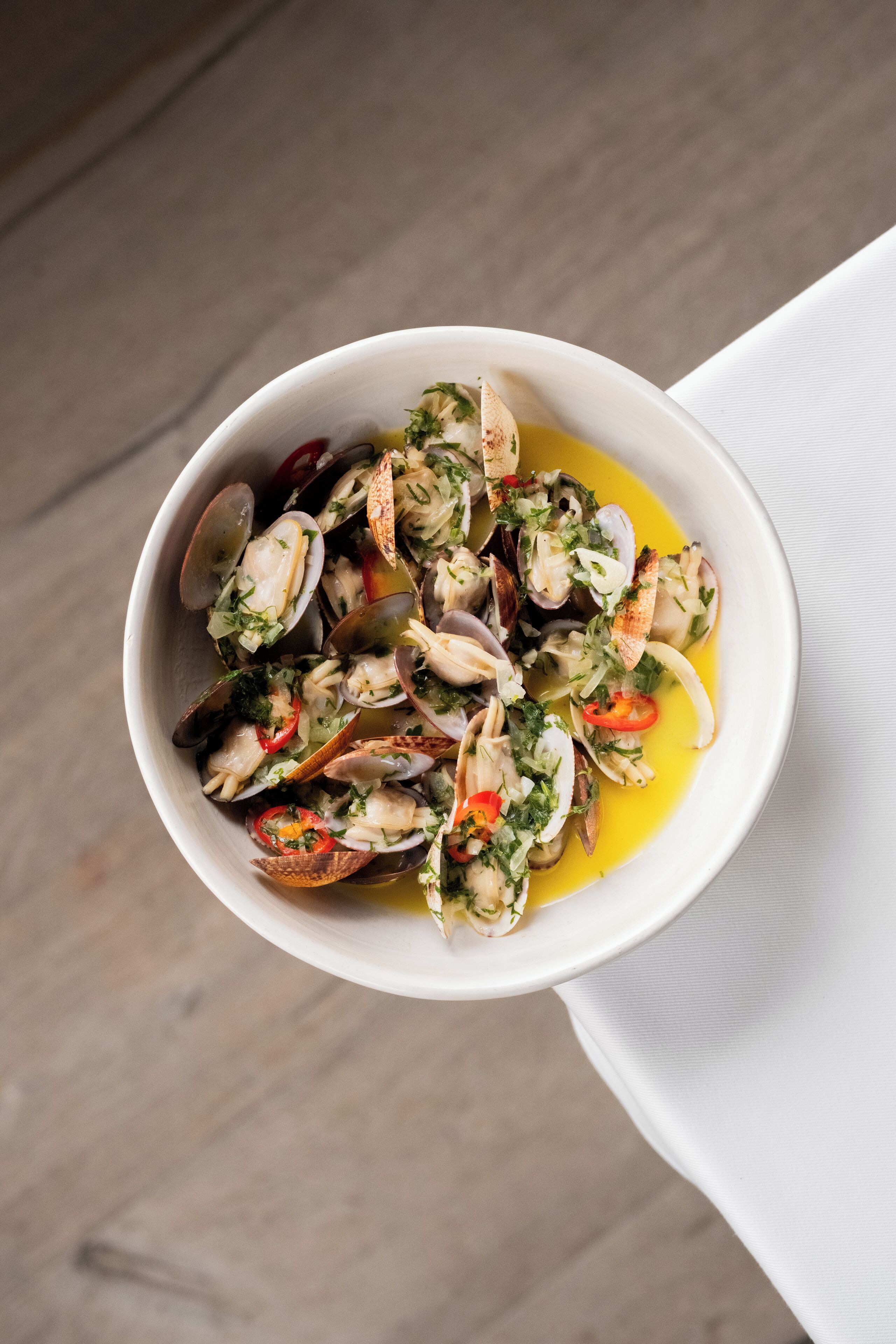 A bowl of clams with herbs and lemon.