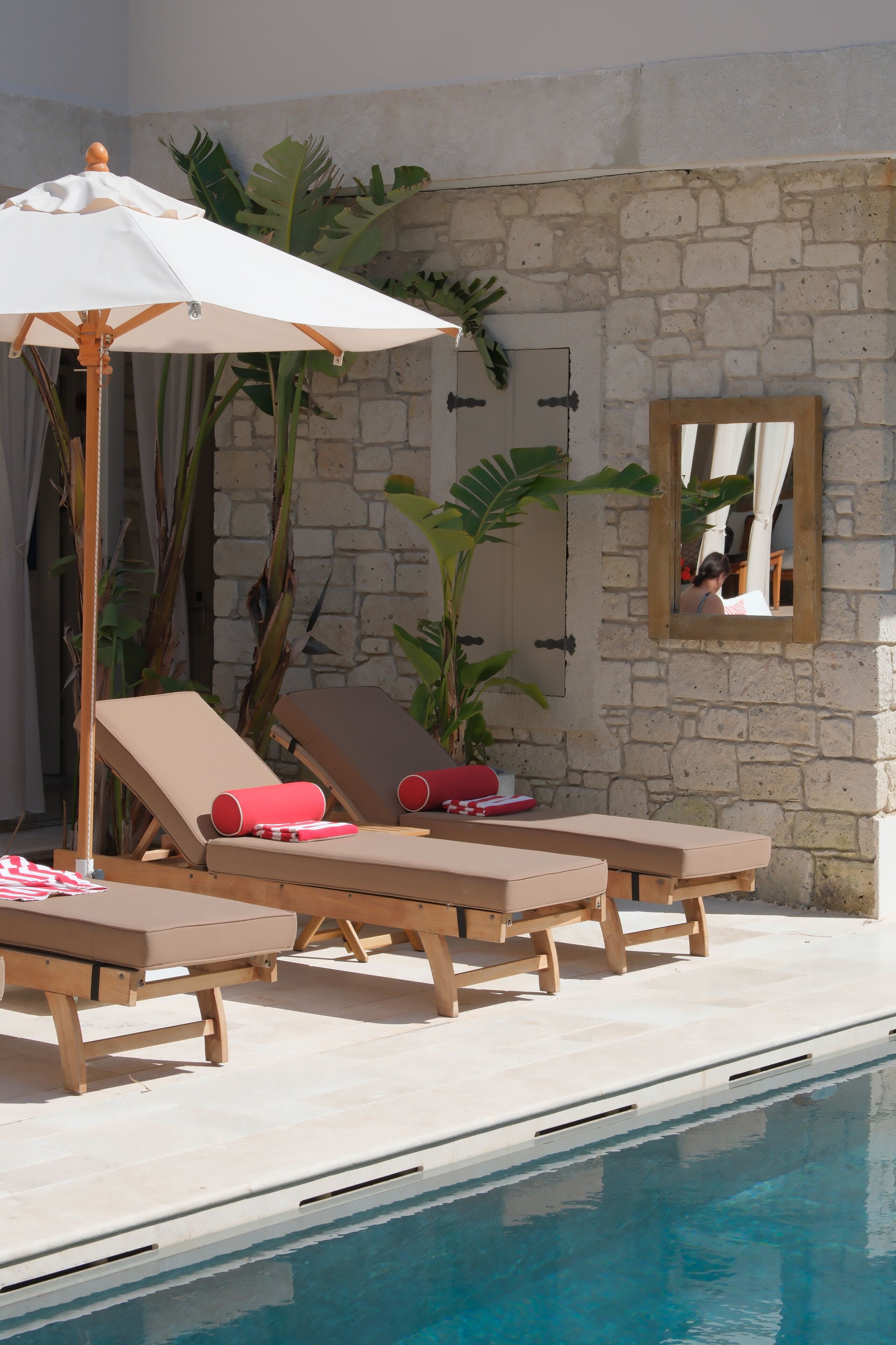 Ein Poolbereich mit Liegestühlen, einem Holz Sonnenschirm und einer Steinmauer.