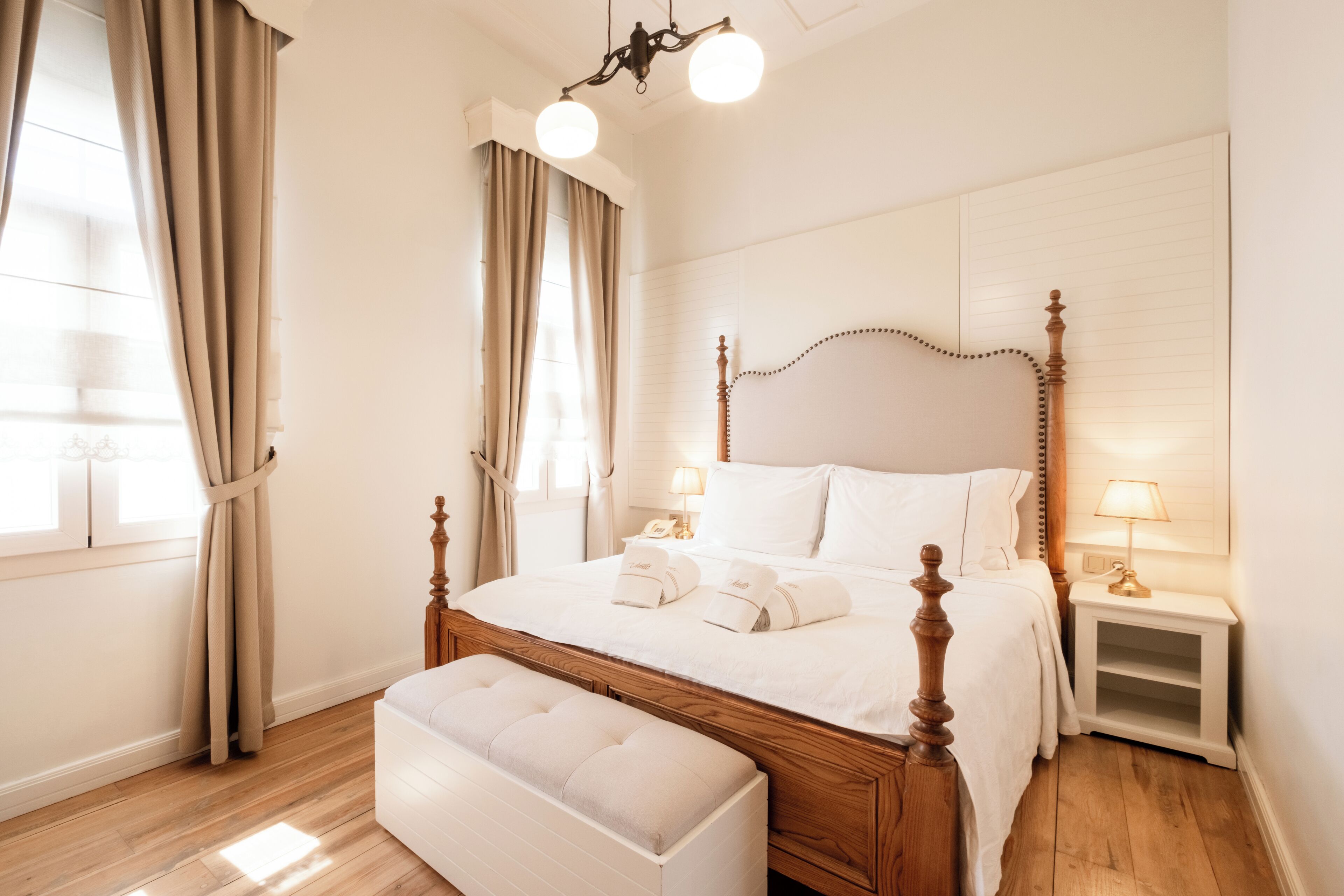 A neatly arranged bedroom with a wooden bed, bedside lamps, and a bench.