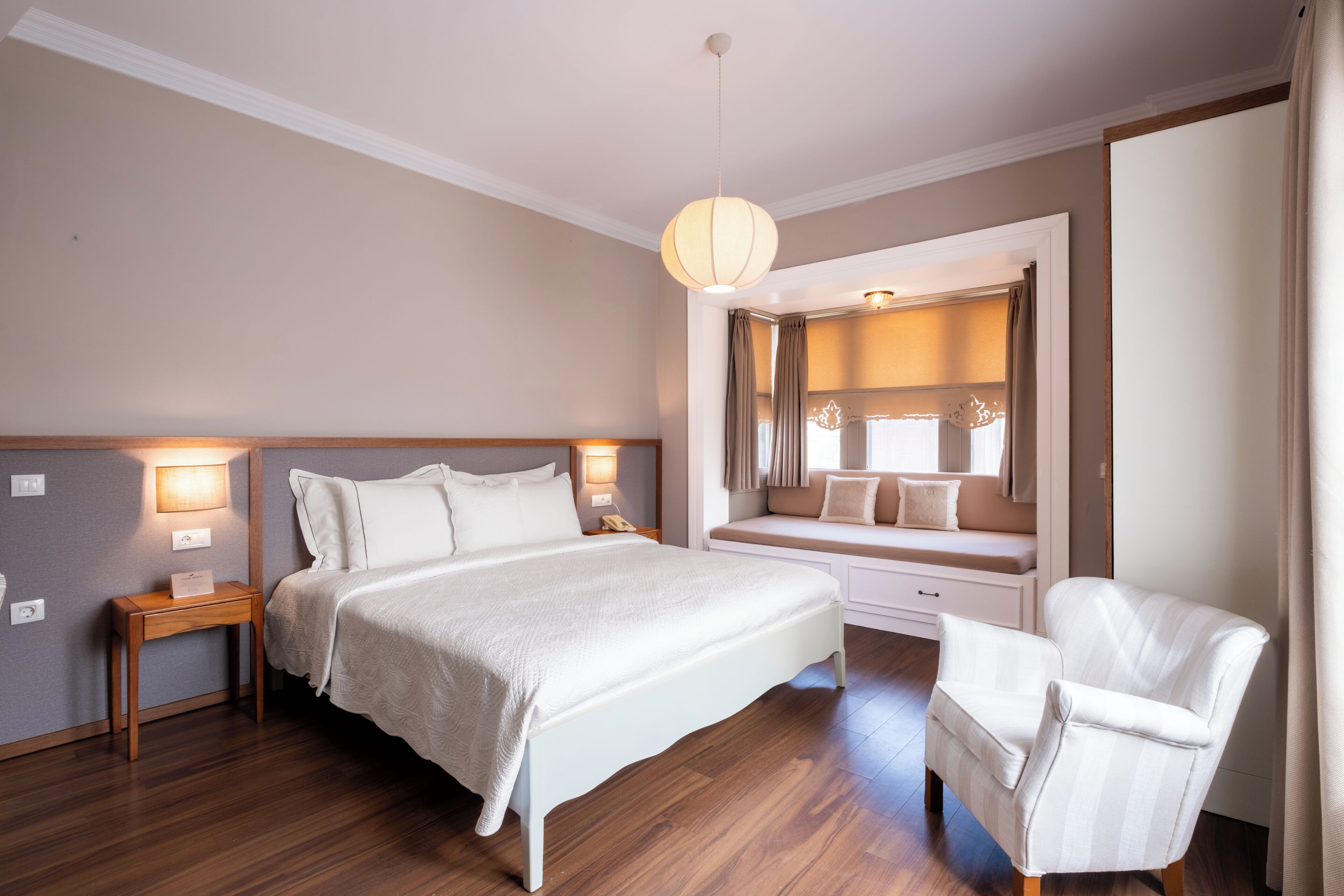 Un dormitorio con una cama grande, mesitas de noche, una silla, un banco con cojines y un espejo.