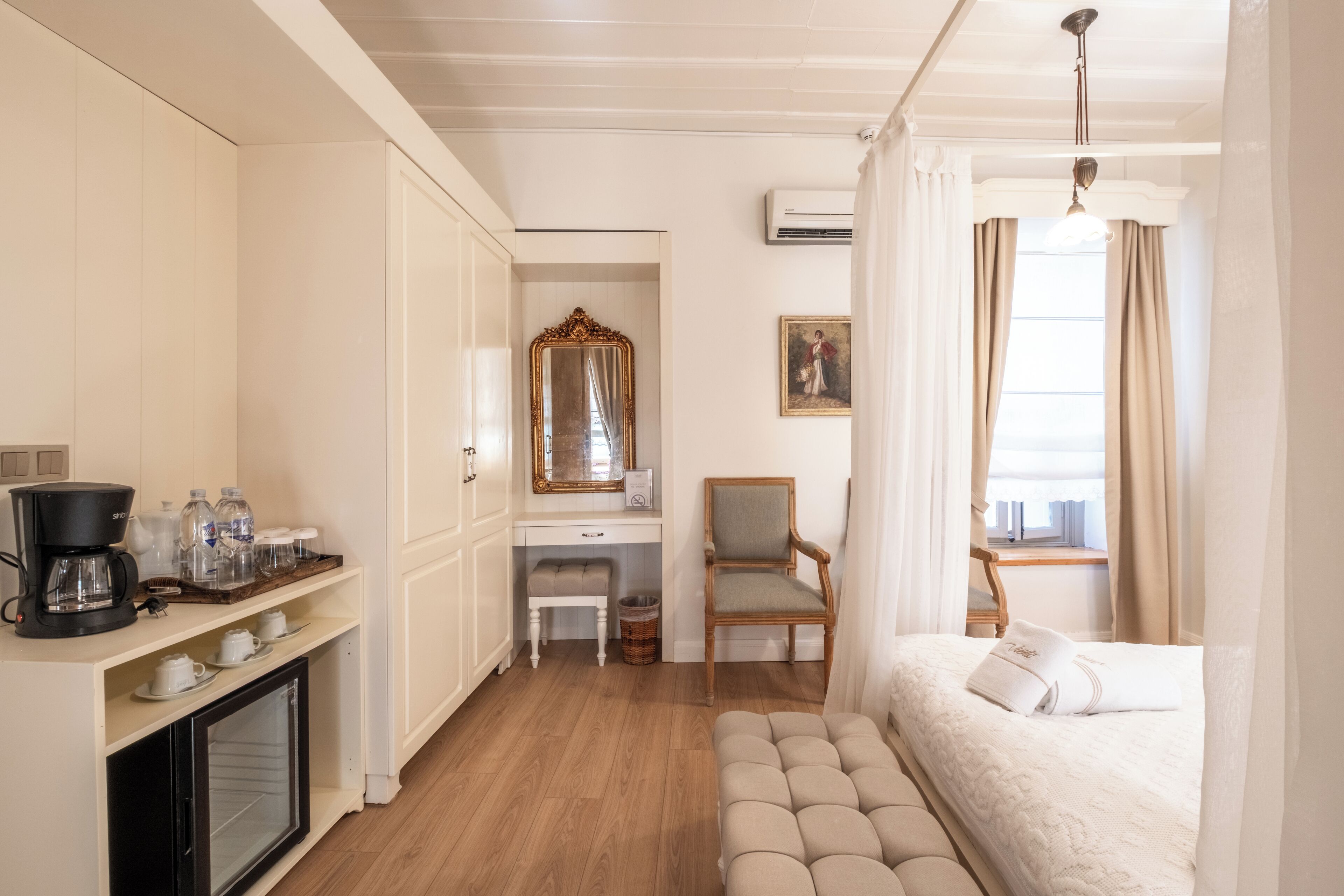 Habitación de hotel con cama, escritorio, silla, espejo, máquina de café y minibar.
