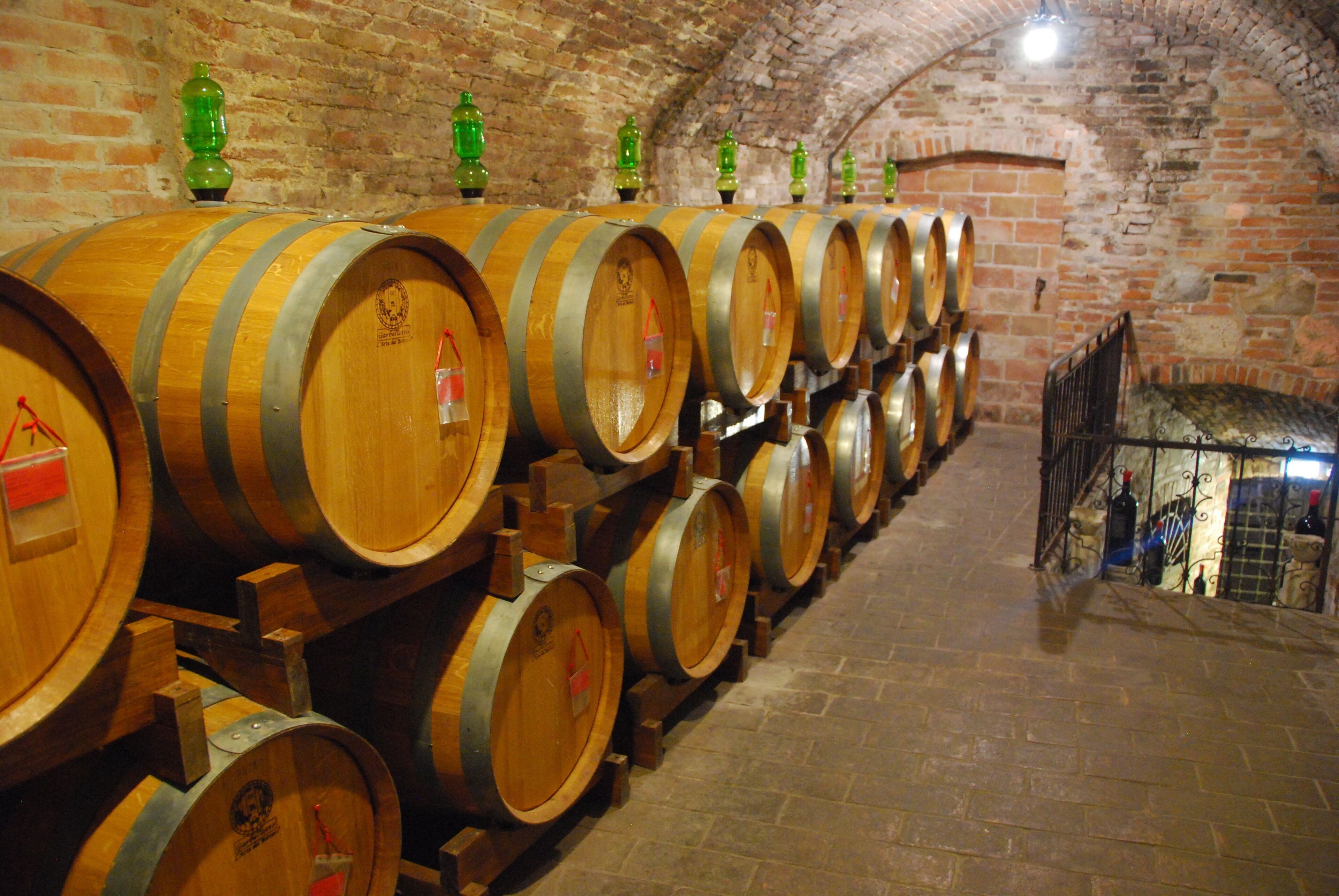 Wooden wine barrels stacked in a cellar with brick walls and a stone floor.