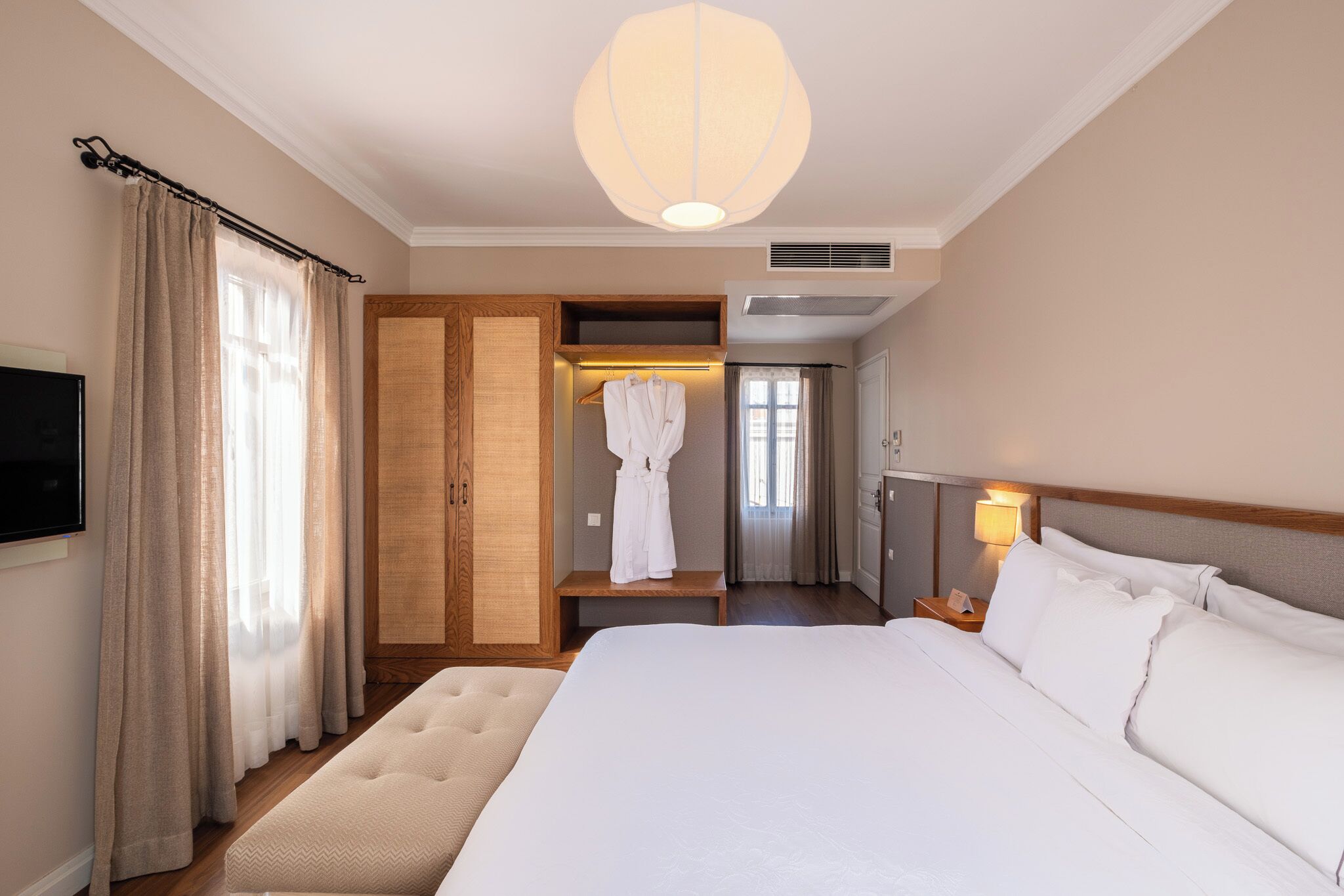 A hotel room with a large bed, a robe rack, a television, and a ceiling light fixture.