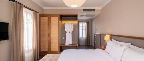 A hotel room with a large bed, a robe rack, a television, and a ceiling light fixture.