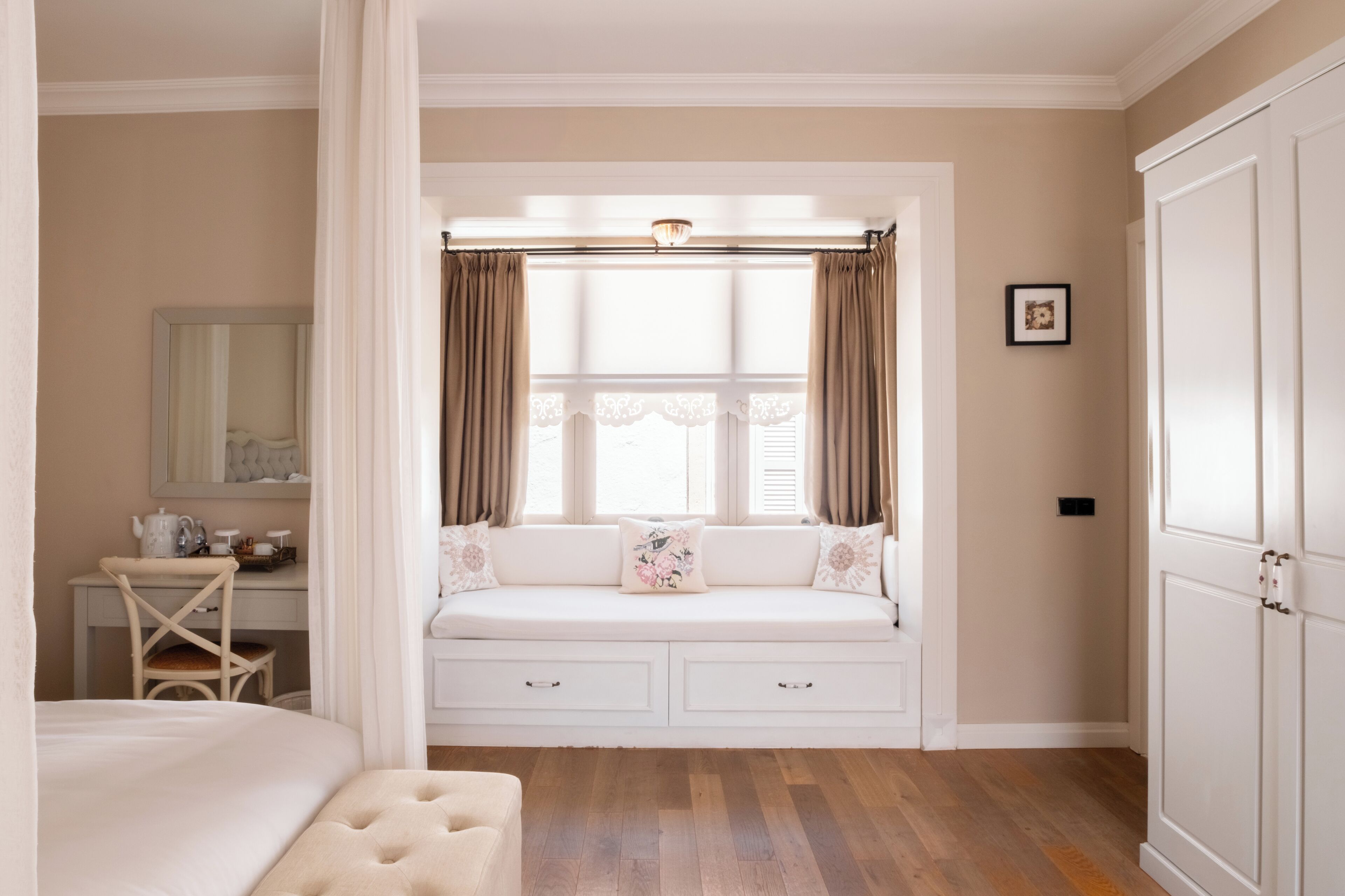 A bedroom with a built-in window seat, a bedside table, a mirror, and a wardrobe.