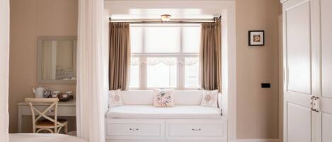 A bedroom with a built-in window seat, a bedside table, a mirror, and a wardrobe.