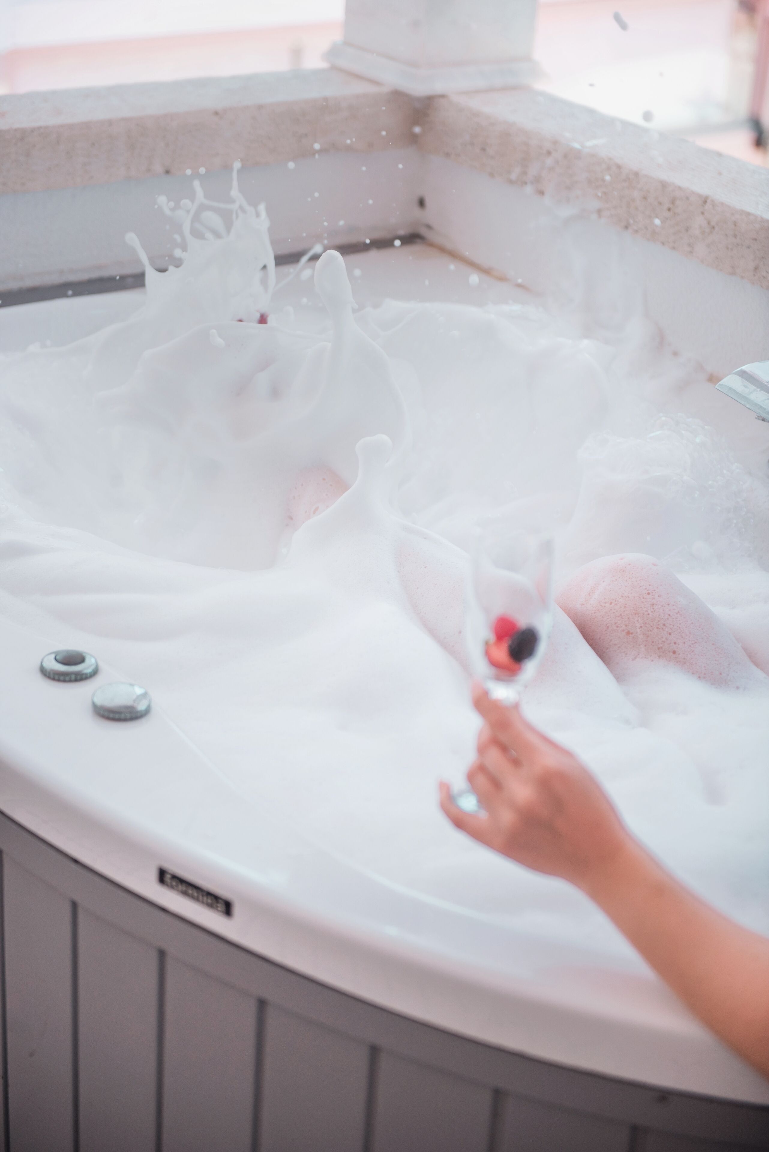 A hot tub with a person holding a glass.