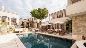 A pool area with lounge chairs and umbrellas, a stone wall, and a tree. - Viento Hotel Alacati - Special Class (Cesme)