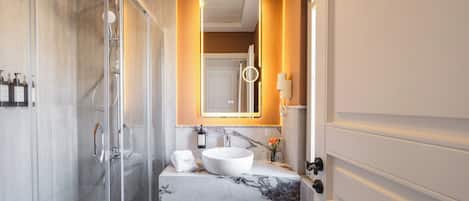 A modern bathroom with a glass-enclosed shower, a marble sink, and a mirror with integrated lighting.