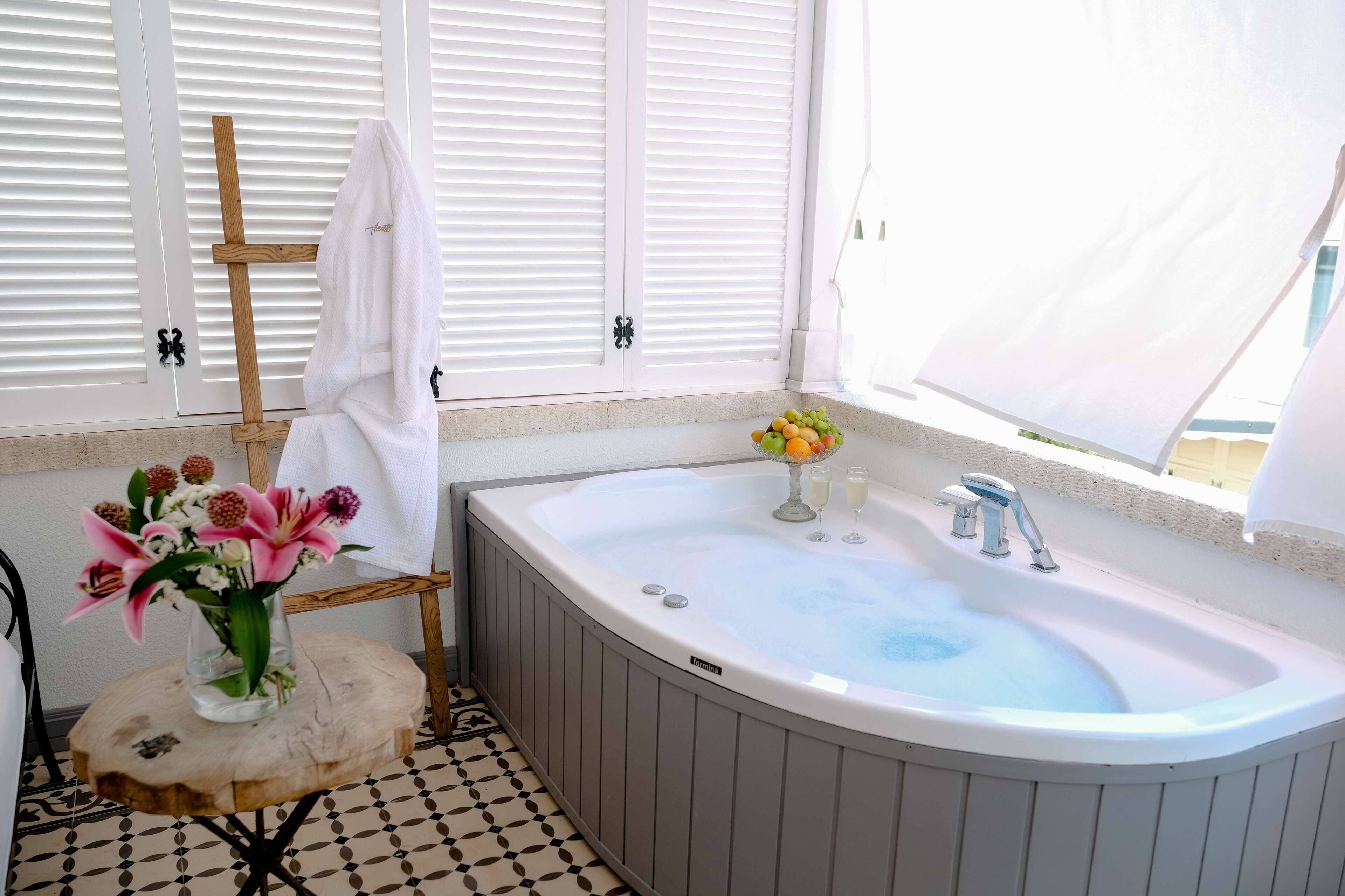 A bathroom with a bathtub, a sink, and a window with blinds.