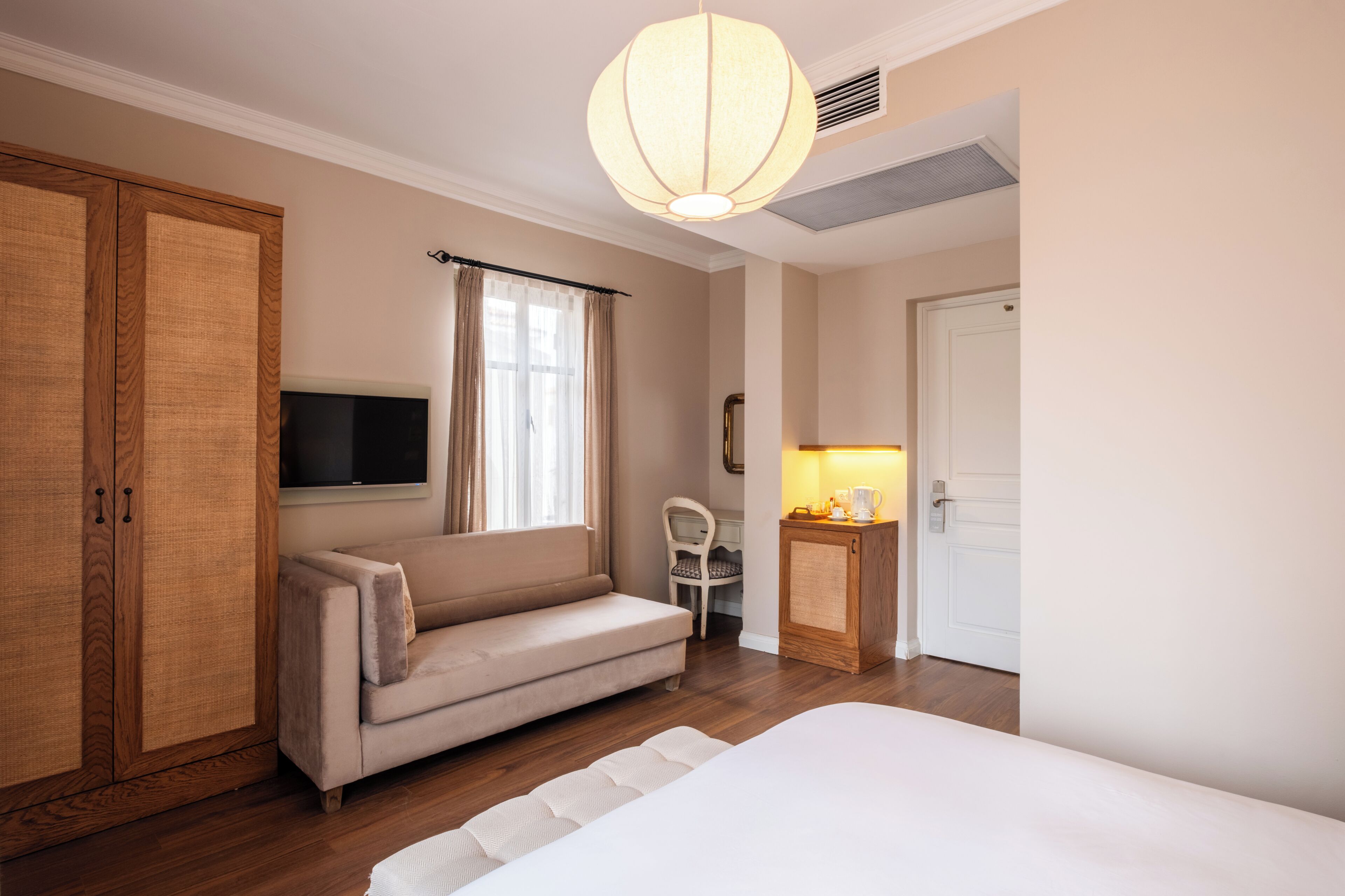 A hotel room with a sofa, a bed, a television, a cabinet, and a door.