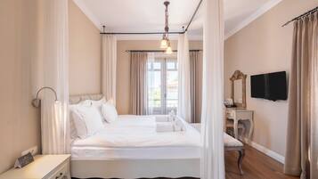 Ein geräumiges Schlafzimmer mit einem großen Bett, einem Nachttisch, einem Schreibtisch, einem Stuhl, einem Fernseher und einem Fenster mit Vorhängen.