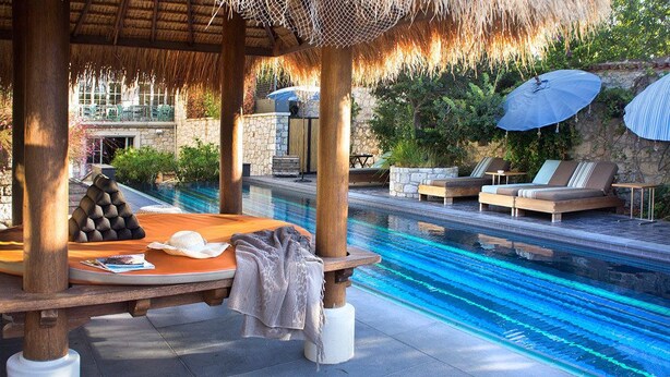 A poolside area with lounge chairs, a wooden table, and umbrellas.