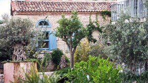 A rustic building with a tiled roof, a blue window, and lush greenery.