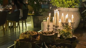 A dining area with wooden chairs, a stone planter with candles, and a table with a candle holder.