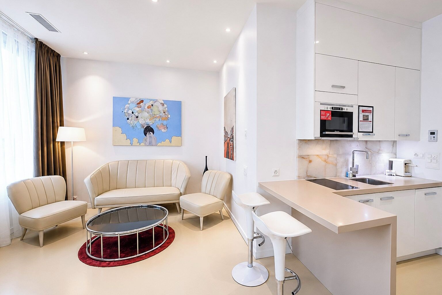 A modern hotel room with a sofa set, a dining area, and a kitchen with a microwave and coffee maker.