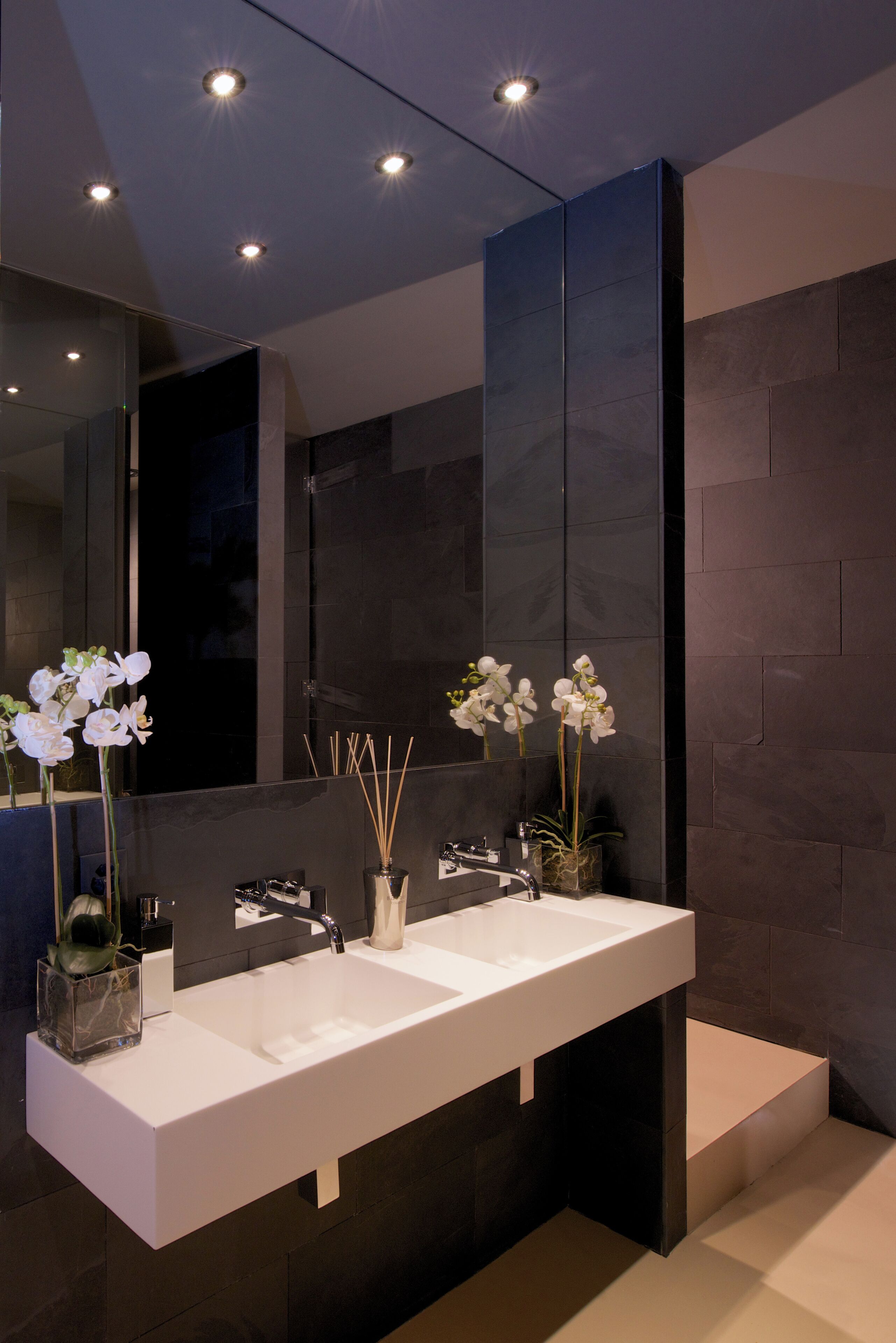 A modern bathroom with a large mirror, two sinks, and decorative orchids.