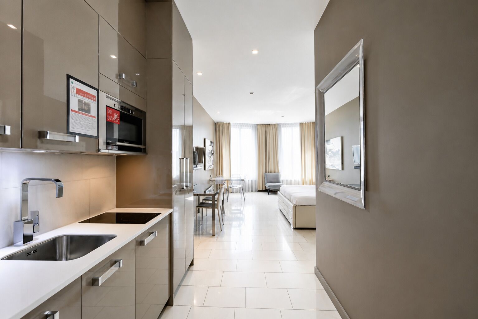 A modern hotel room with a kitchenette, a dining area, and a large mirror.