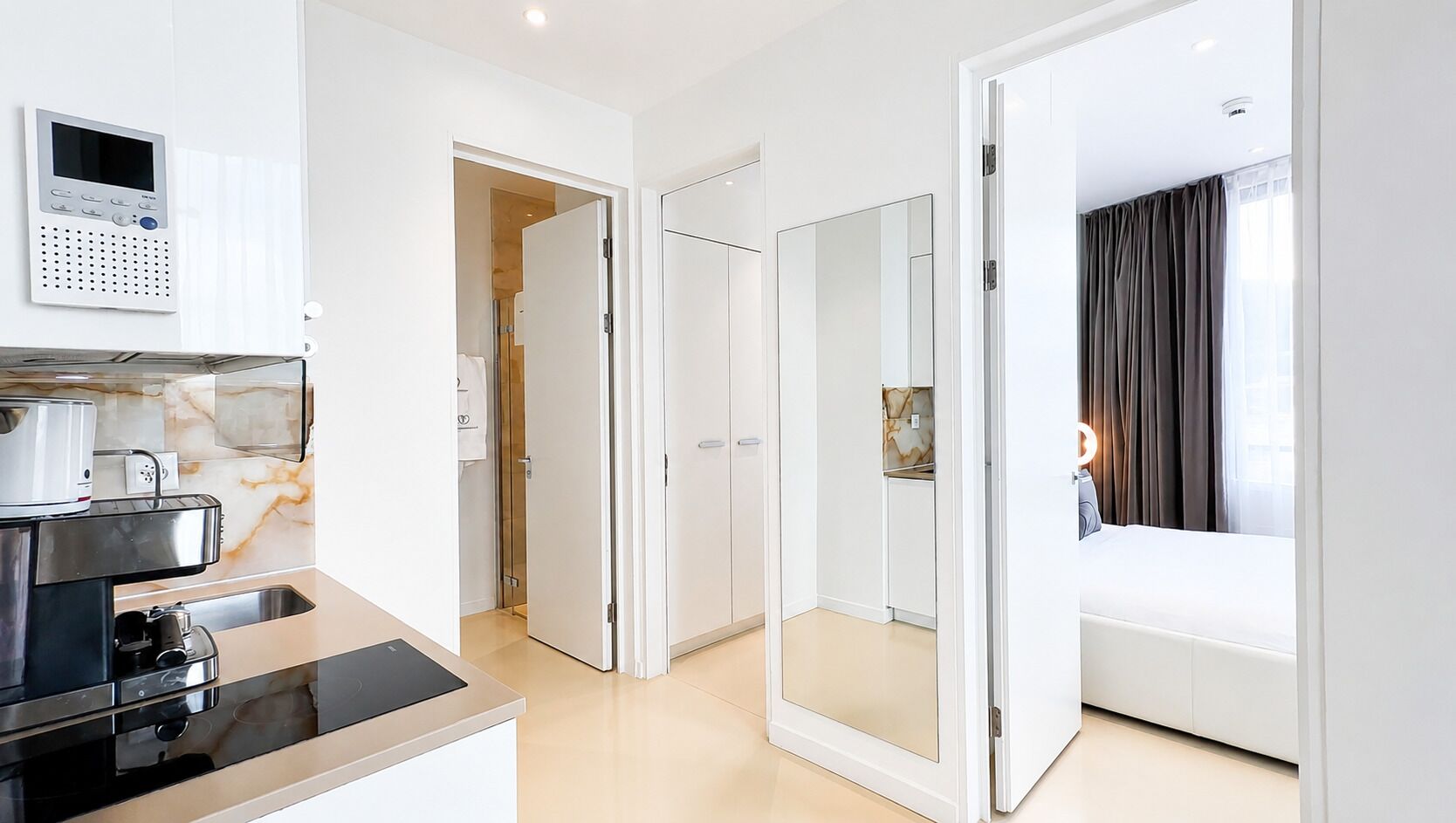 A modern hotel room with a kitchenette, a large mirror, and a bed.