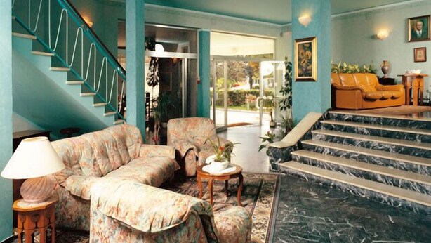 A spacious living area with a sofa, a coffee table, and a staircase leading to an outdoor area. - Hotel Helvetia (Grado)