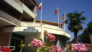 A hotel named "HOTEL HELVETIA" with a sign on the building. There are flags on poles in front of the hotel. - Hotel Helvetia (Grado)