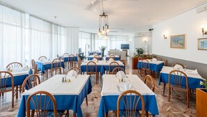 A dining area with tables set for service, large windows, and a ceiling fan. - Hotel Helvetia (Grado)