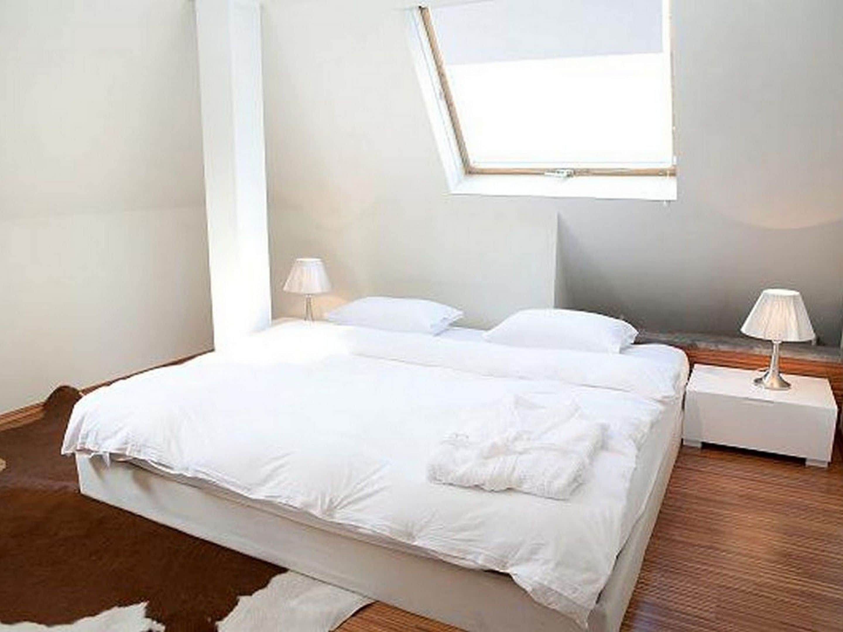 Une chambre avec un grand lit, deux tables de chevet et une lucarne.