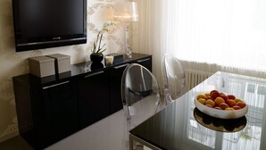 A modern hotel room with a flat-screen TV, a dining table with chairs, a bowl of fruit, and a decorative lamp. - VISIONAPARTMENTS Zurich Waffenplatzstrasse (Zürich)