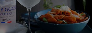 Una botella de vodka Grey Goose y un plato de pasta con un vaso de agua.