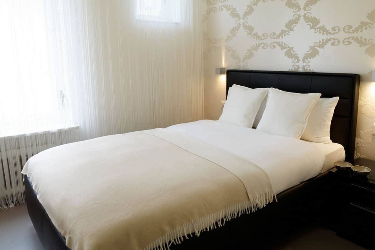 Un lit bien fait, avec une tête de lit sombre, du linge de lit blanc et un motif décoratif sur le mur.