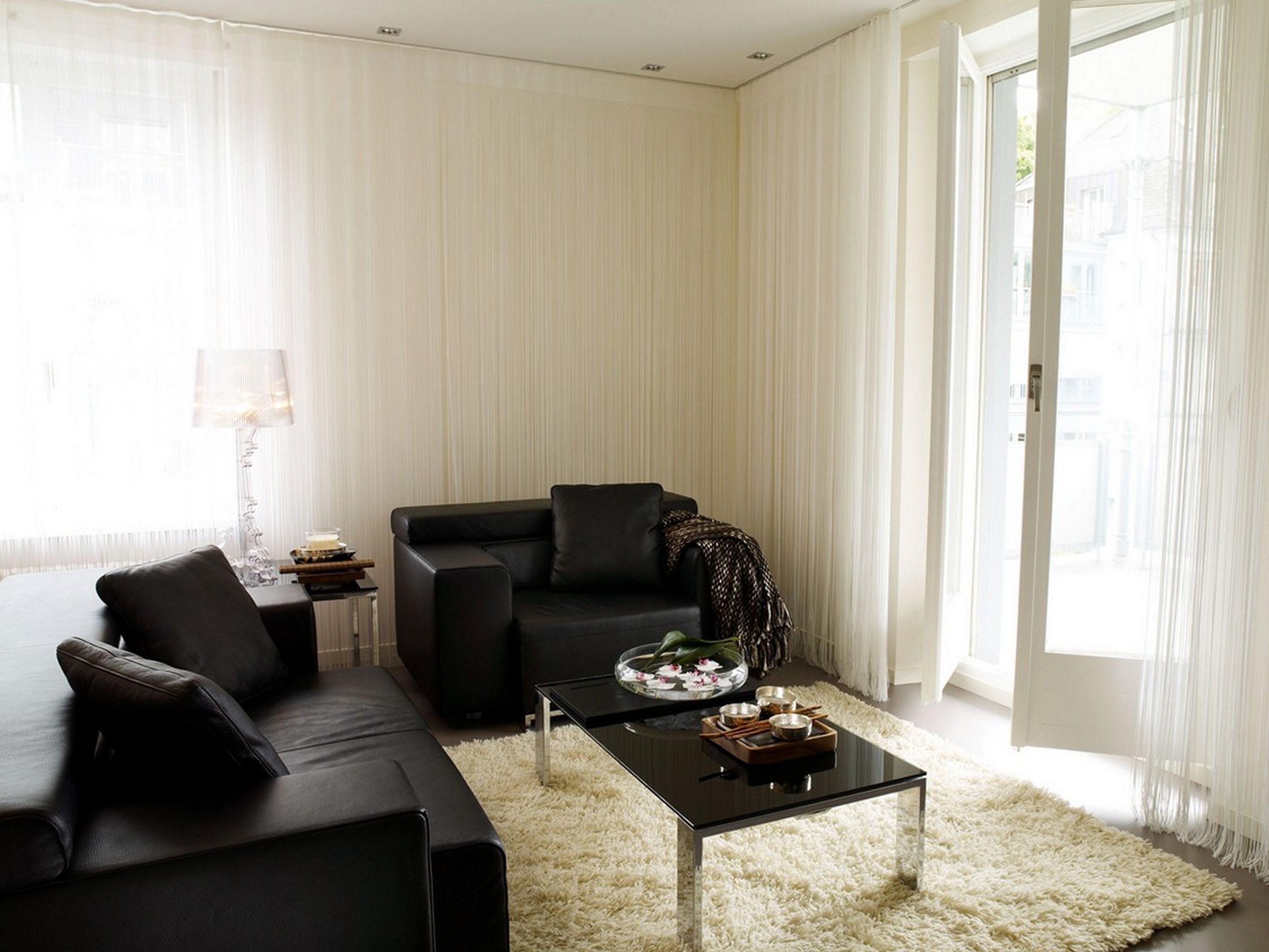 En moderne stue med en sort sofa, et glasbord og en tyk, hvid løber.