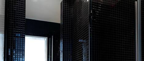 Un bany modern amb un lavabo blanc, parets revestides de rajola negra i un espai de dutxa amb envàs de vidre.