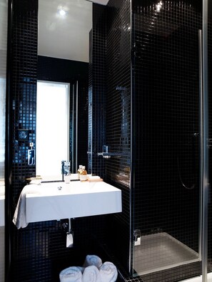 Un baño moderno con un lavabo blanco, paredes con azulejos negros y una mampara de cristal para la ducha.